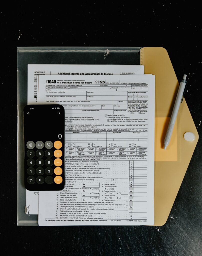 Formulários de imposto, calculadora e caneta sobre mesa, representando a retenção de impostos na nota fiscal de serviço